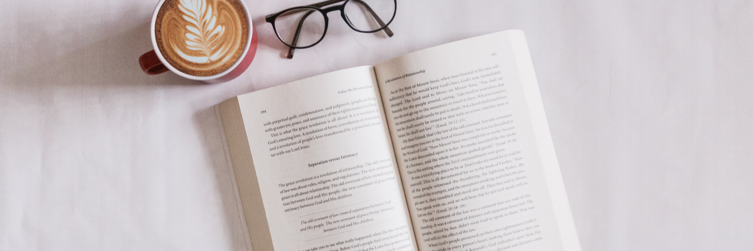 banner of an open book with a pair of glasses and a coffee next to it on a white tabletop